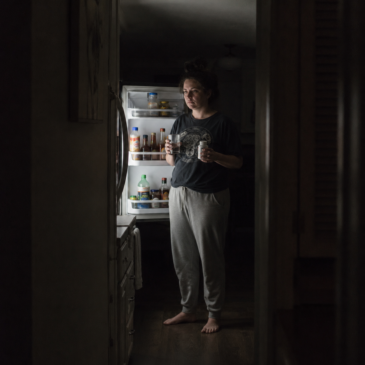 Woman awake in the kitchen in the middle of the night, unable to sleep from back pain