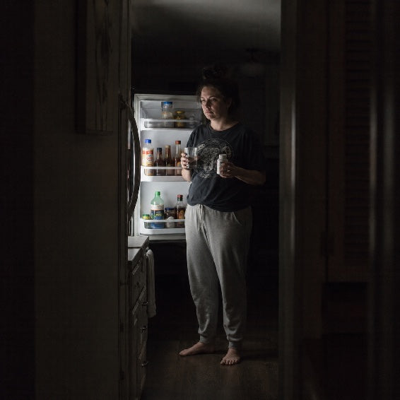 Woman awake in the kitchen in the middle of the night, unable to sleep from back pain